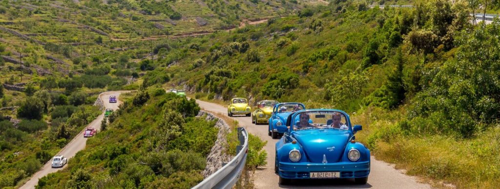 Convoy of colourful vintage cars on a winding road through the Adriatic countryside