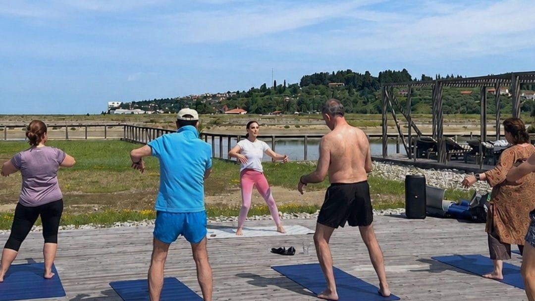 A group doing yoga on a wooden deck at Lepa Vida, with the Sečovlje salt pans behind